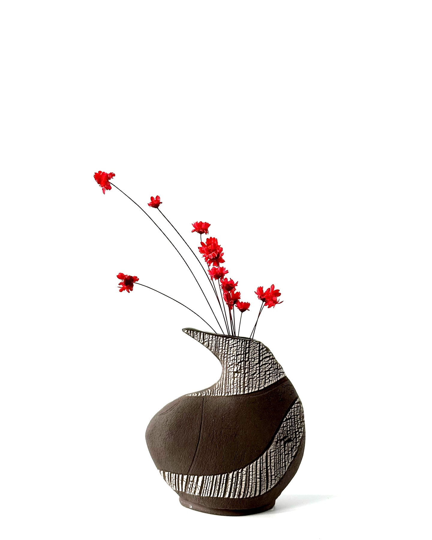 Decorative vase with black and white pattern and red flowers on a white background